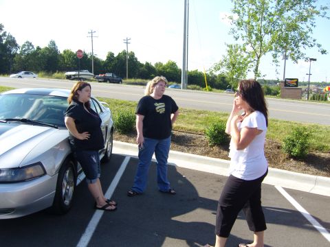 2007 Ford Mustang - A silver 2007 Ford Mustang is parked in a lot with three women standing around it.