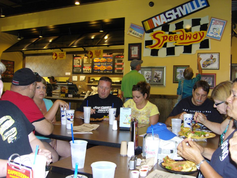 People sit at tables in a restaurant decorated with Nashville Speedway checkered flags and racing imagery