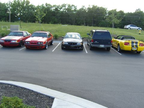2007 Ford Mustang - A yellow convertible Mustang with black racing stripes is parked in a lot with other vehicles.