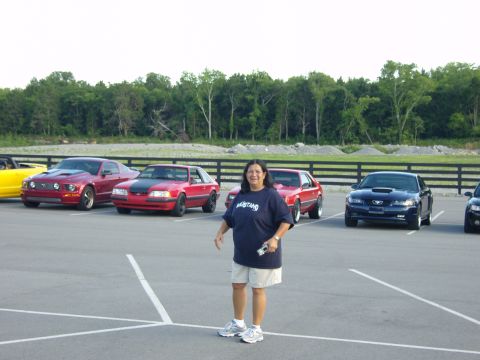 2007 Ford Mustang - Several Ford Mustangs are parked in a lot with a woman standing in front of them.