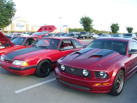 2007 Ford Mustang - Two red Ford Mustangs, one a 2007 model and the other a 1990s model, are parked in a lot.