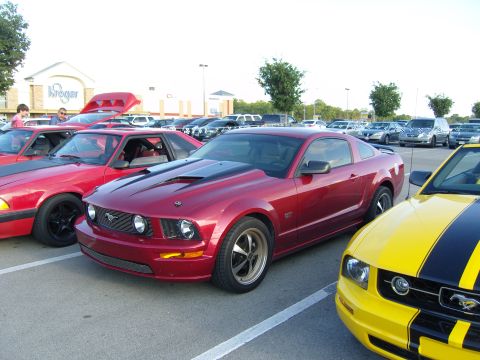 2007 Ford Mustang - A red 2007 Ford Mustang GT is parked in a lot with other vehicles, including a yellow Mustang.