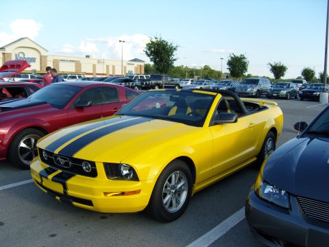 2007 Ford Mustang - A yellow convertible Ford Mustang with black racing stripes is parked in a lot near a Kroger store.