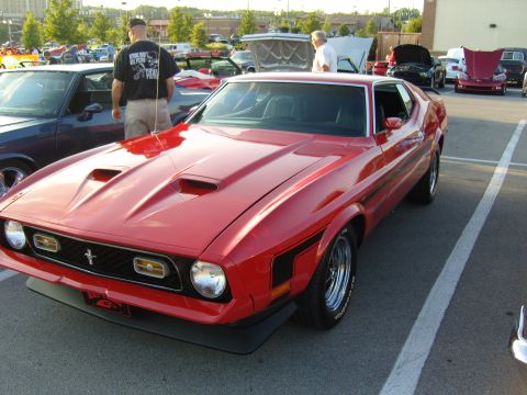 2007 Ford Mustang - A red classic Ford Mustang is parked at a car meet with other vehicles in the background.