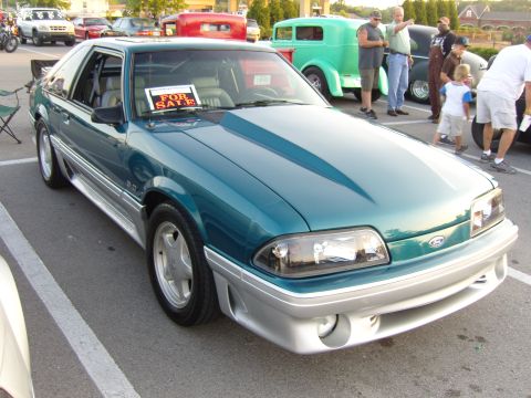 2007 Ford Mustang - A teal coupe with silver trim is parked at an outdoor car show, with a 'For Sale' sign visible on the dashboard.