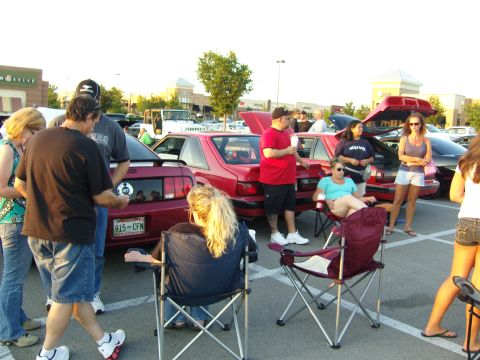 2007 Ford Mustang - A group of people attend a car meet, with several red Ford Mustangs on display.