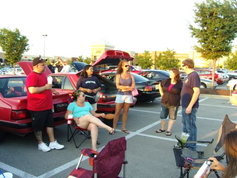 2007 Ford Mustang - A group of people socialize around vehicles parked in a lot during an outdoor gathering.