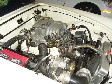 2007 Ford Mustang - Close-up view of a V8 engine bay, a 5.0L engine and a red battery. Another vehicle is visible in the background.