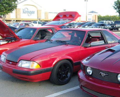 2007 Ford Mustang - Several red Ford Mustangs are parked in a lot, one with its hood open.