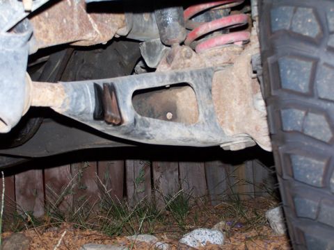 1990 Ford Bronco - Undercarriage view showing suspension parts and a tire, with a wooden fence in the background.