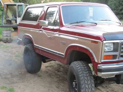 1984 Ford Bronco - This lifted Ford Bronco features a two-tone red and tan paint scheme and is positioned near construction equipment.