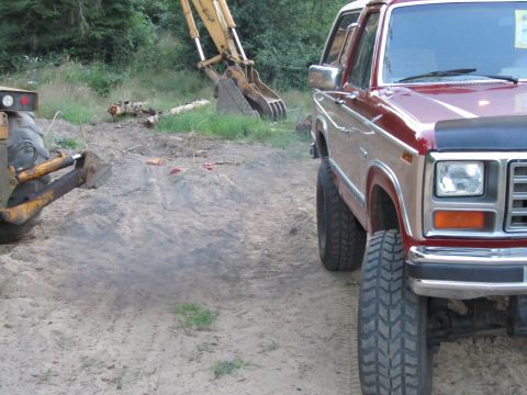 1984 Ford Bronco - A lifted Ford Bronco sits on a dirt lot next to construction equipment.