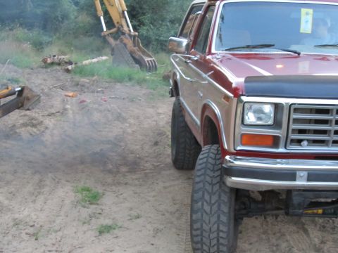 1984 Ford Bronco - Red and tan 1984 Ford Bronco parked outdoors near construction equipment.