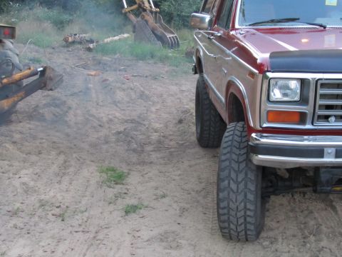 1984 Ford Bronco - This lifted Ford Bronco is parked on a dirt lot with construction equipment in the background.