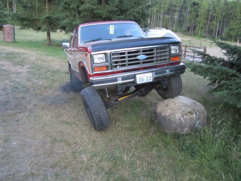 1984 Ford Bronco - Ford Bronco off-roading, kicking up black smoke while climbing over a large rock.