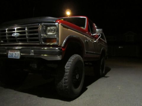 1984 Ford Bronco - A red and tan Ford Bronco is parked at night, viewed from the front three-quarter angle.