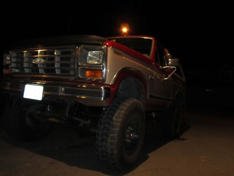 1984 Ford Bronco - This red and tan Ford Bronco is shown from the front 3/4 angle at night.
