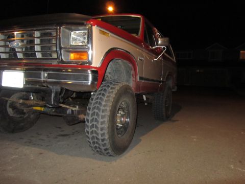 1984 Ford Bronco - Two-tone red and tan Ford Bronco with off-road tires and suspension visible.