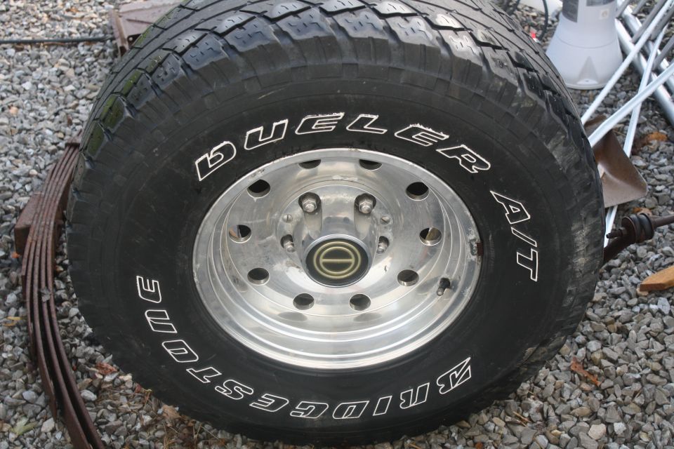Bridgestone Dueler A/T tire on a chrome wheel with a leaf spring nearby