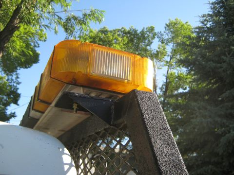 1972 Ford F-250 - An amber emergency light bar is mounted on a vehicle, viewed from a low angle against a clear blue sky and foliage.
