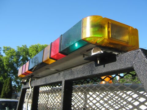 1972 Ford F-250 - Multicolor amber, green and red emergency light bar mounted on a black mesh truck bed rack against a blue sky.