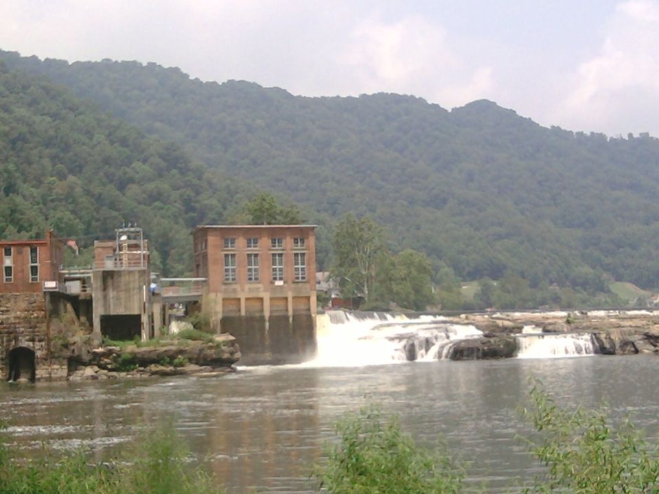 Hydroelectric dam with brick buildings and a waterfall on a river, with a forested mountain in the background