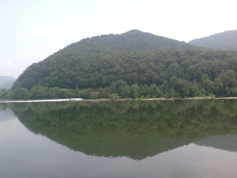 1985 Ford Crown Victoria LTD - A landscape a calm lake mirroring a dense, tree-covered mountain range.