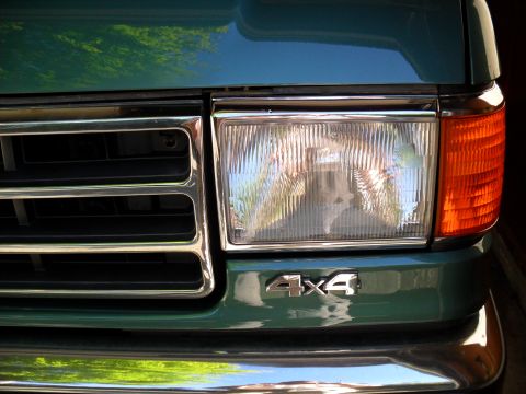 1990 Ford Bronco - Close-up of the front of a green 1990 Ford Bronco, showing the grille, headlight, and 4x4 badge.