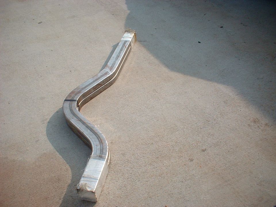 S-curved bare steel rectangular tube frame rail section lying on concrete