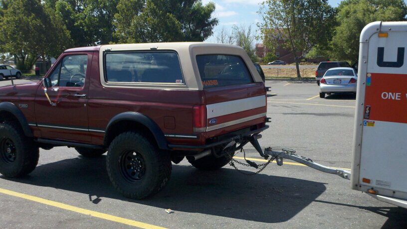 Maroon Ford Bronco with a tan removable top, towing a U-Haul trailer