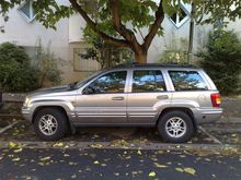 1991 Ford Crown Victoria - A silver 1999 Jeep Grand Cherokee is parked on the side of the road, with a building and trees in the background.