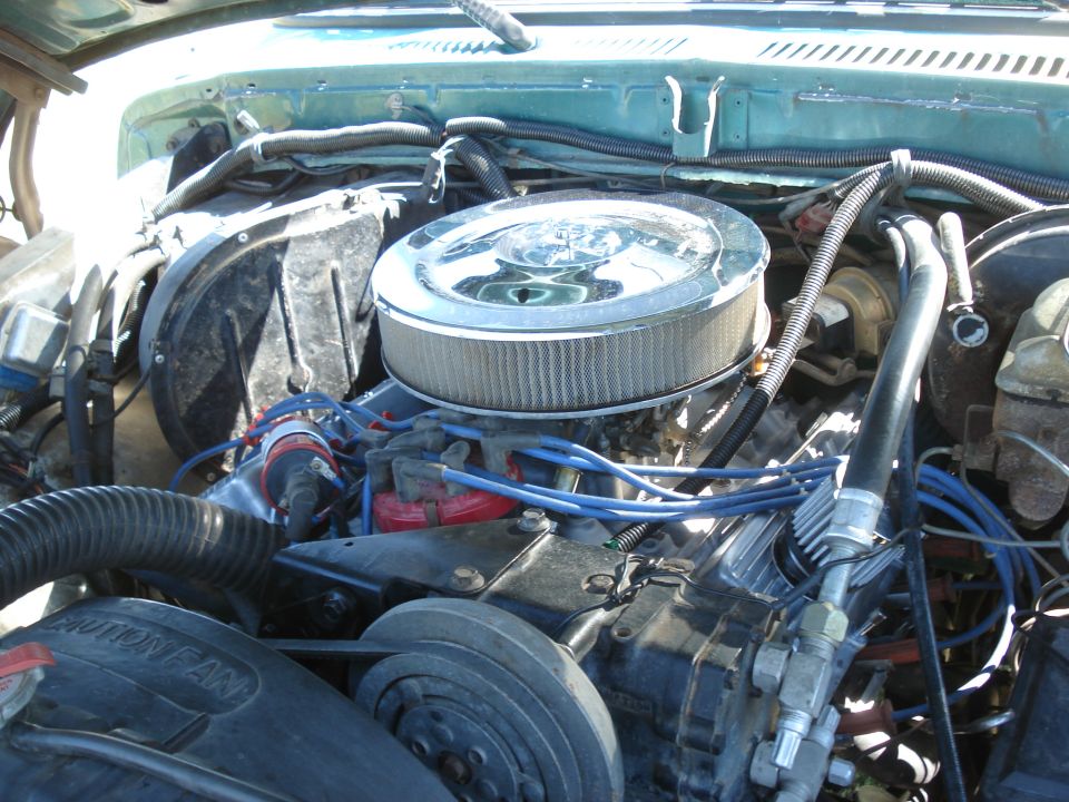 Engine bay with chrome air cleaner, blue spark plug wires, and a fan. Text on fan reads 'CAUTION FAN'