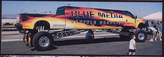 Side view of a lifted truck with "BLUE MEDIA VEHICLE GRAPHICS" flame livery