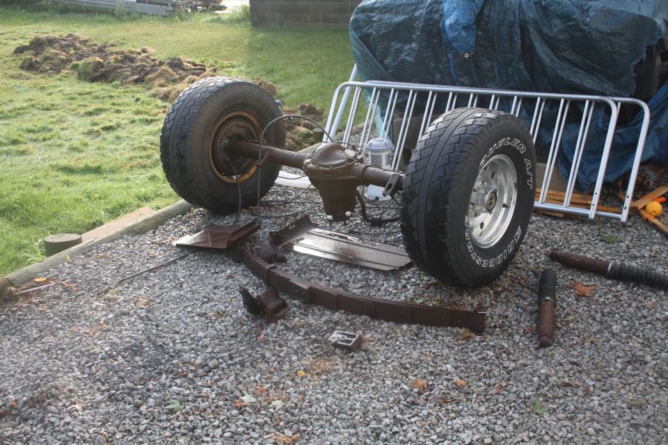 Rear axle assembly with leaf springs and shocks, sitting on gravel