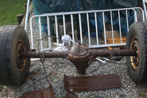 1996 Ford Bronco - A disassembled rear axle assembly with tires and brake lines sits on gravel, suggesting a vehicle tear-down.