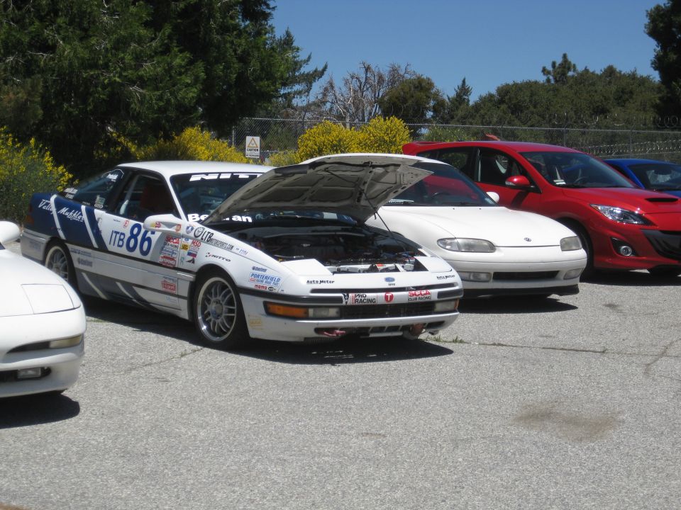 White 1990 Ford Probe race car with blue decals and number 86, hood open, parked on asphalt