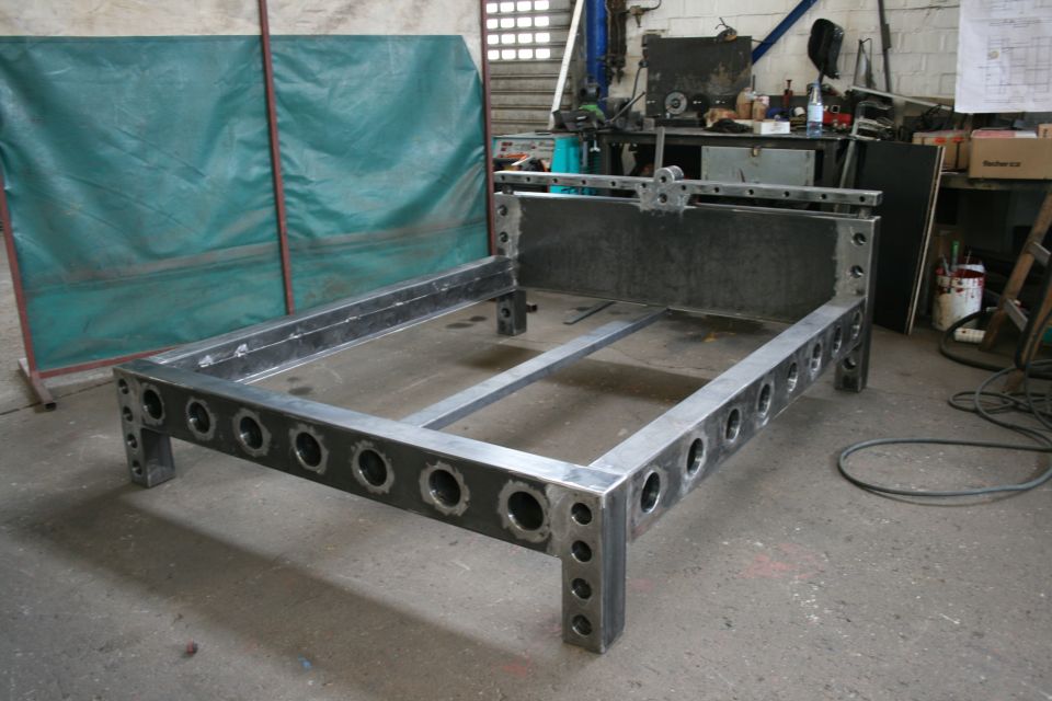 Metal bed frame with circular cutouts on legs, in a workshop setting