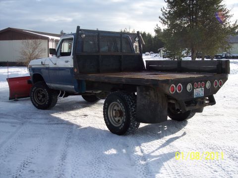 1973 Ford F-250 - This blue and white flatbed truck, identified as a 1973 Ford F-250, is equipped with a snow plow and seen in a snowy environment.
