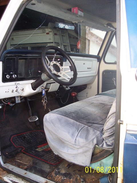 1973 Ford F-250 - The interior of a 1973 Ford F-250 reveals a white dashboard, an aftermarket steering wheel, and a grey seat cover.