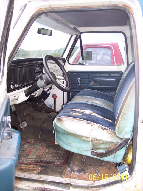1973 Ford F-250 - The interior of a truck shows worn striped seats and a floor mat. A second truck is visible through the window.