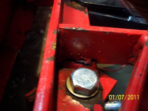 1973 Ford F-250 - Extreme close-up of a chipped red-painted steel bracket welded into a red frame channel, secured by a large plated hex bolt with a thick wa…