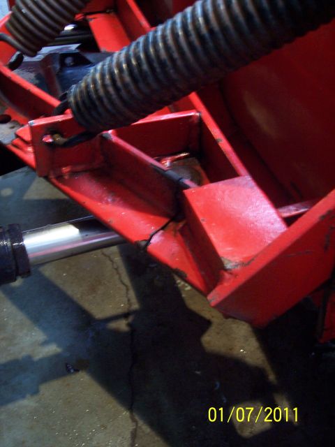 1973 Ford F-250 - Red-painted snowplow frame and A-frame gussets photographed on a concrete shop floor, with a heavy coil trip spring at top and a chrome hyd…