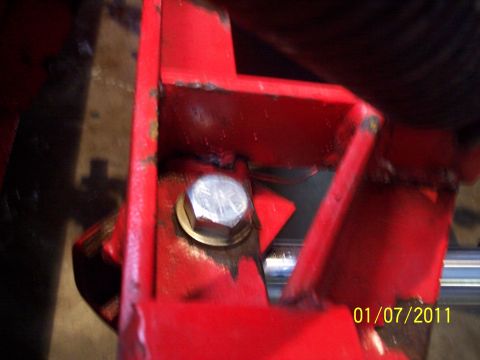 1973 Ford F-250 - Close-up of a red-painted fabricated steel bracket assembly with a welded gusset, fastened by a large zinc-plated hex bolt and brass-colore…