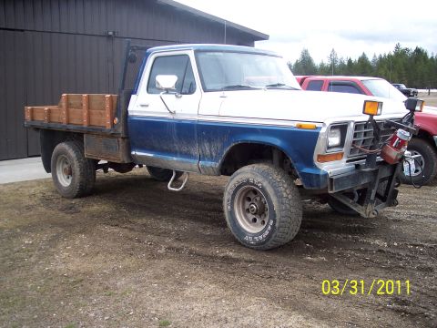 1973 Ford F-250 - Passenger-side three-quarter front view of a blue-over-white 4x4 Ford pickup with a wooden-sided flatbed, headache rack and a front-mounted…