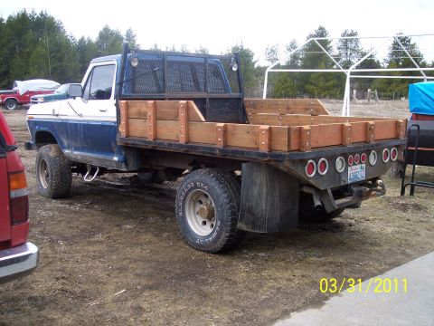 1973 Ford F-250 - Driver-side three-quarter rear view of a blue-over-white lifted 4x4 Ford pickup fitted with a wooden stake-side flatbed, expanded-metal hea…