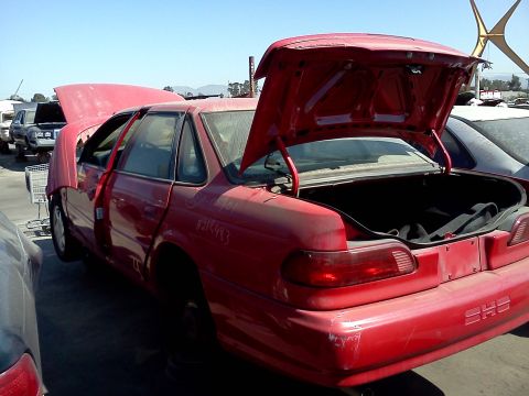 1993 Ford Taurus - This red 1993 Ford Taurus is in a junkyard, with its hood and trunk open, showing the SHS badge on the rear.