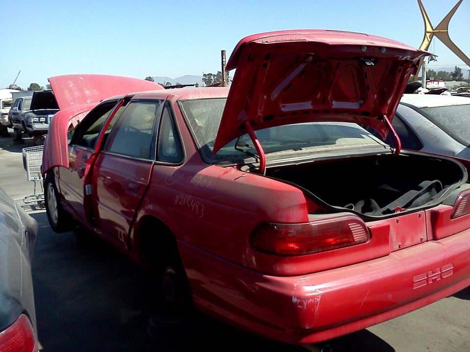 red 1993 Ford Taurus with hood and trunk open in junkyard, SHS badge visible on rear