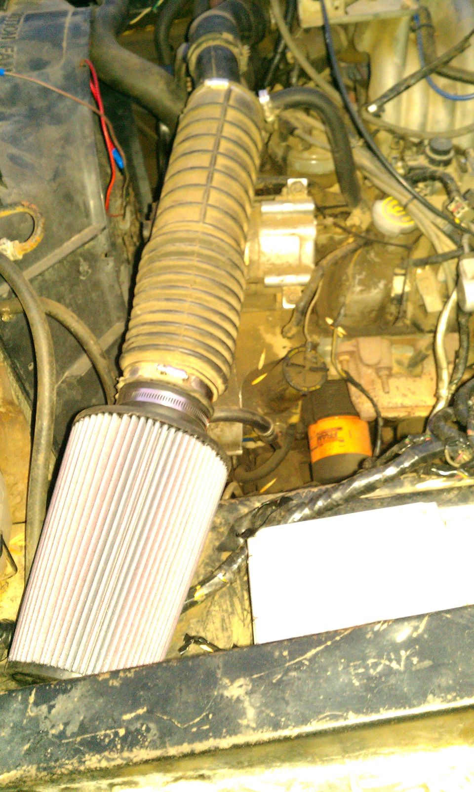 Engine bay showing a large cylindrical air filter connected to a ribbed intake hose. Some hoses and engine components are visible
