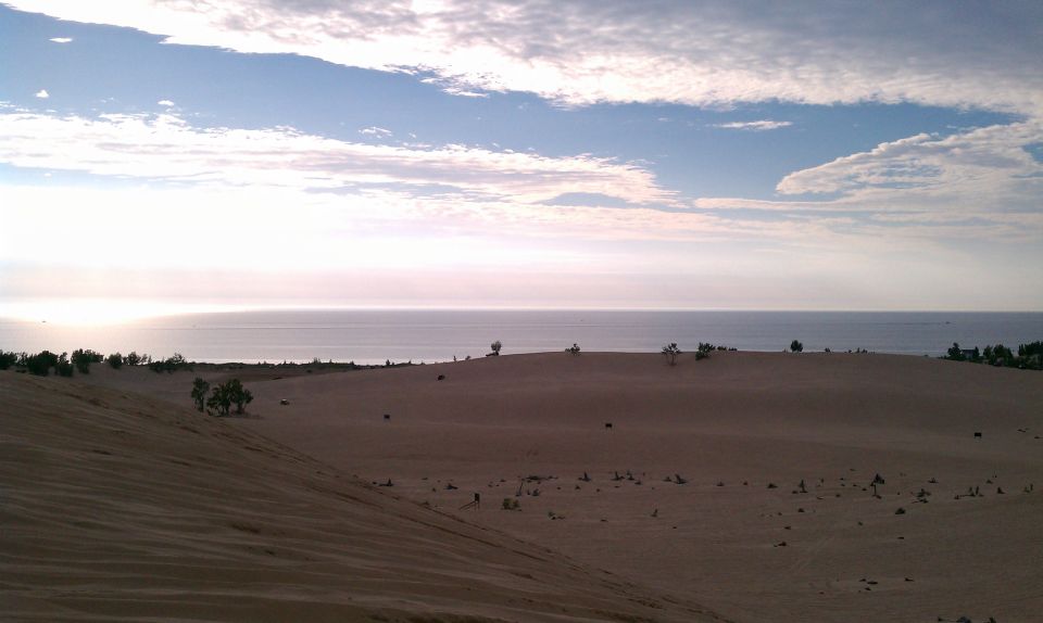 sand dunes stretch towards a calm ocean under a cloudy sky