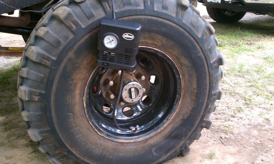 Close-up of a large, mud-caked tire with a black Slime air compressor attached to the wheel hub